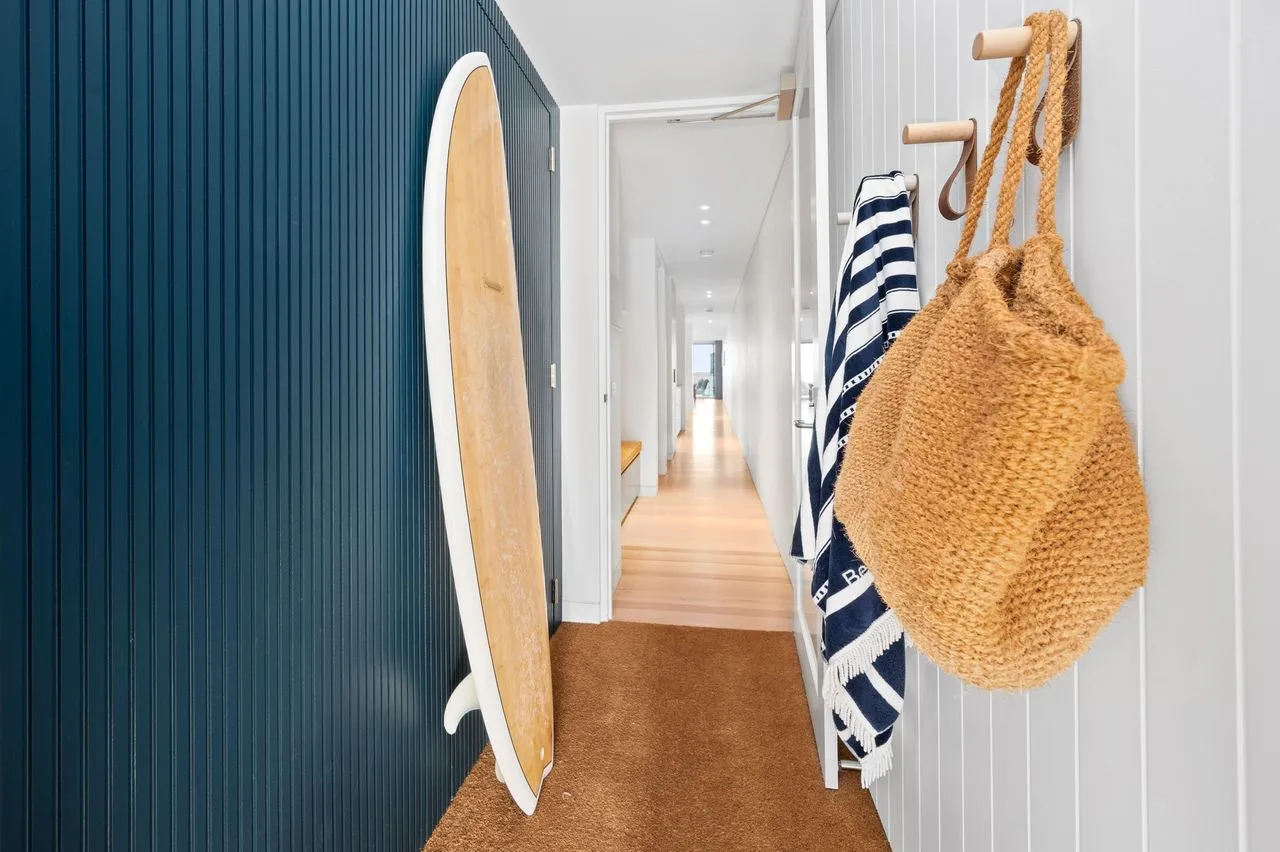 Un pasillo luminoso tiene una tabla de surf apoyada en la pared y toallas colgadas junto a la entrada.