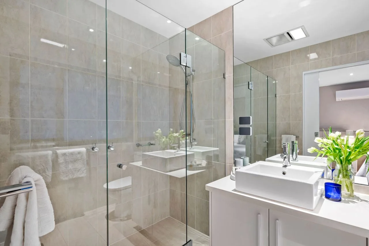 Baño con azulejos, ducha de vidrio y un lavabo con mueble.