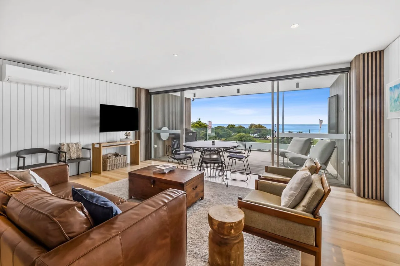 Living room with seating and a wide view through glass doors to the balcony.