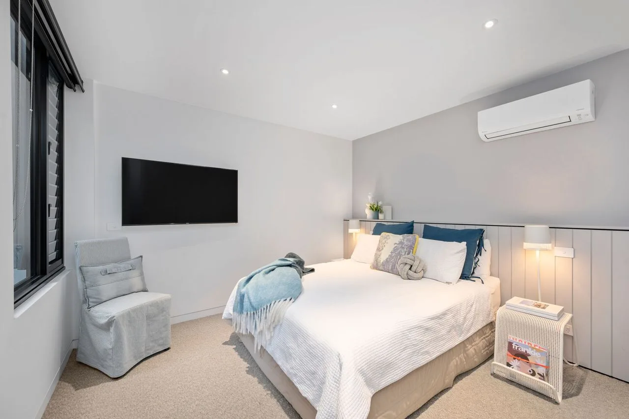 Un dormitorio luminoso con una cama doble, un televisor de pared y lámparas de noche.