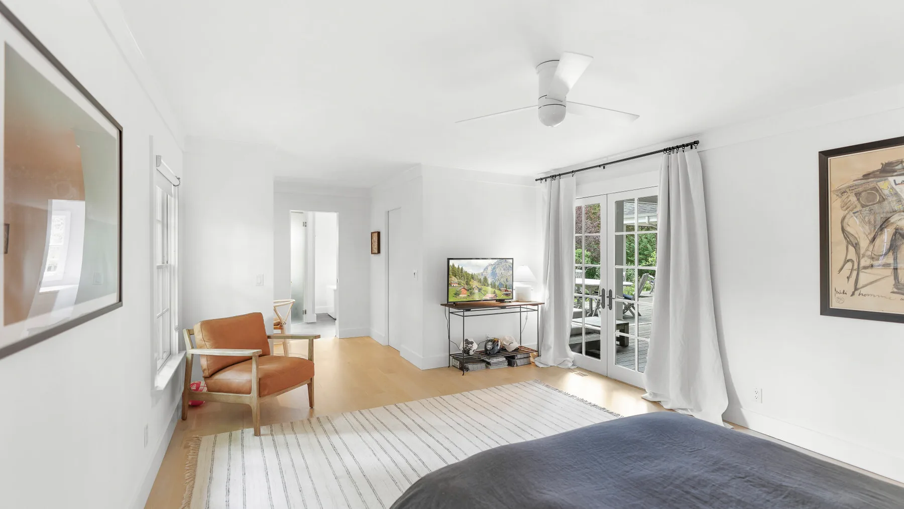 Un dormitorio luminoso con una cama, un sillón y puertas de vidrio hacia un balcón.