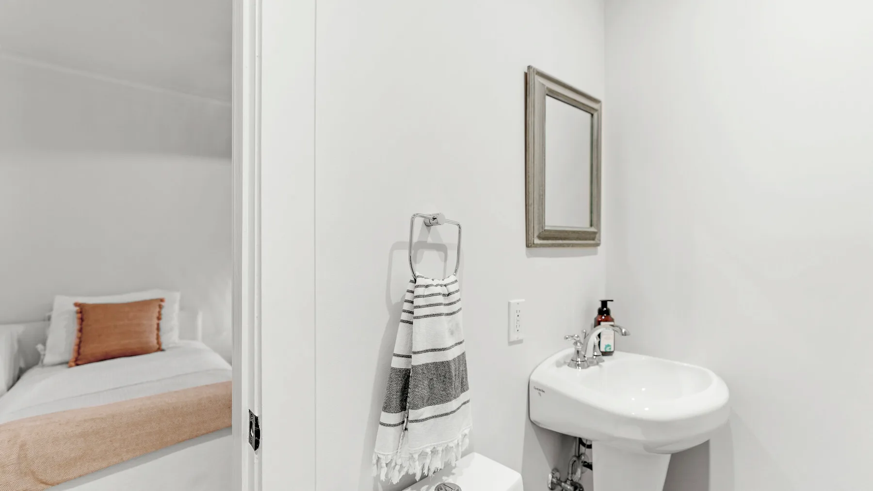 Un dormitorio junto al lavabo del baño, con una cama bien arreglada y una toalla colgada.