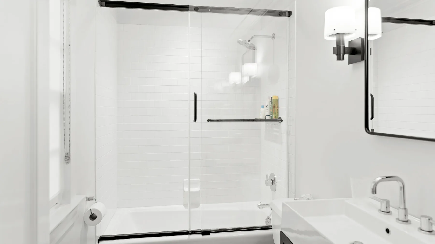 Un baño luminoso con ducha de vidrio y lavabo.