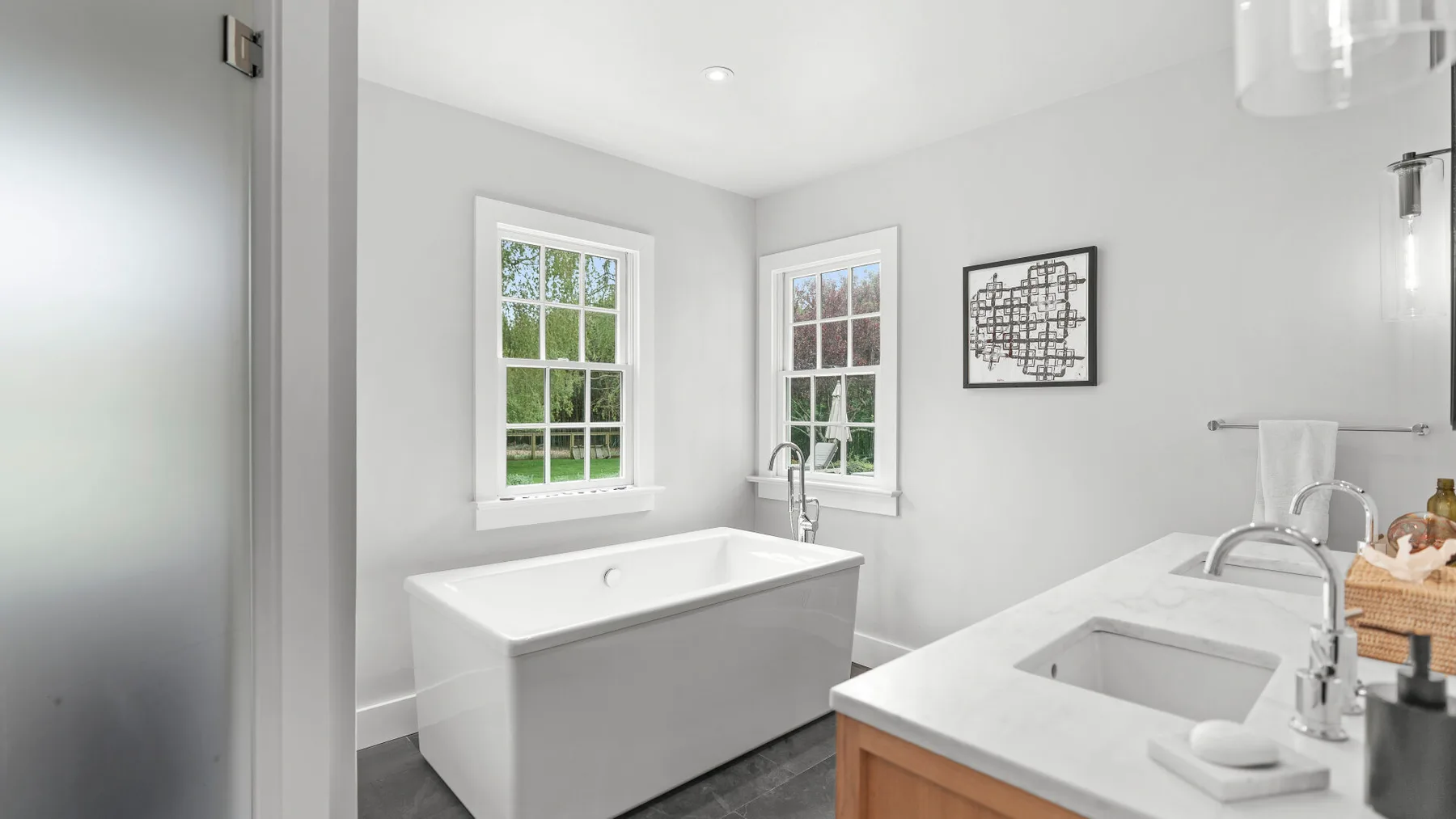 Un baño luminoso con bañera, lavabo y dos ventanas.
