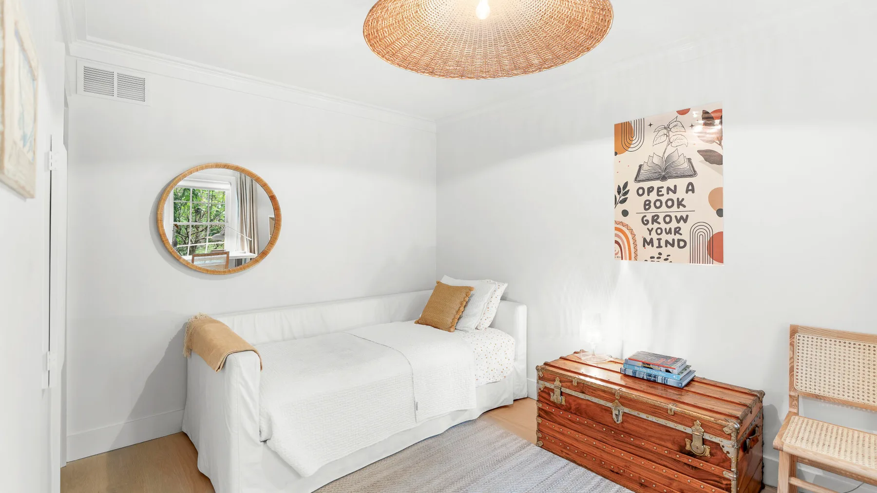 Un dormitorio luminoso con ropa de cama blanca y un baúl de madera junto a la cama.