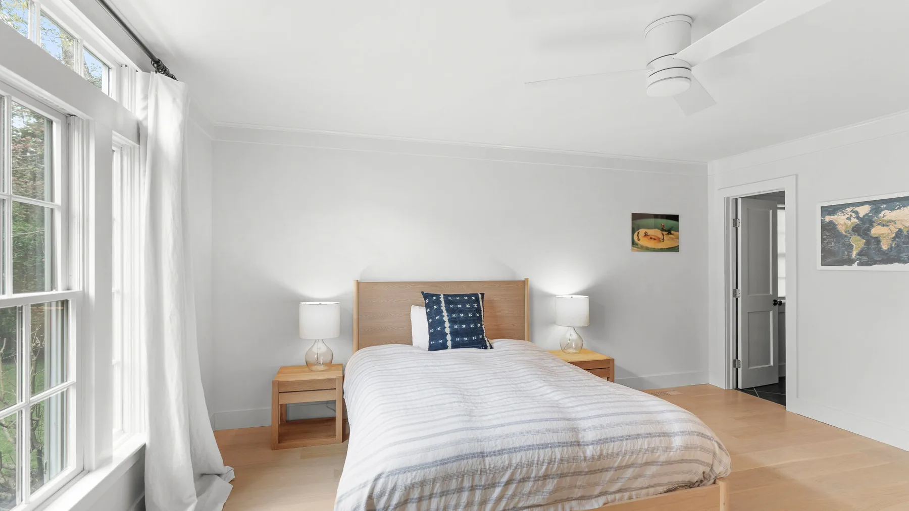 Un dormitorio luminoso con una cama, mesas de noche y grandes ventanas.