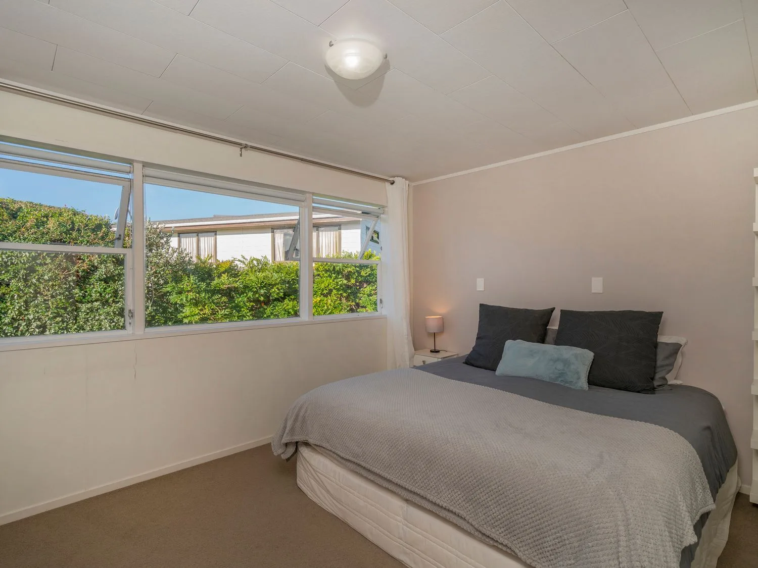 A bedroom with a bed and windows overlooking greenery.