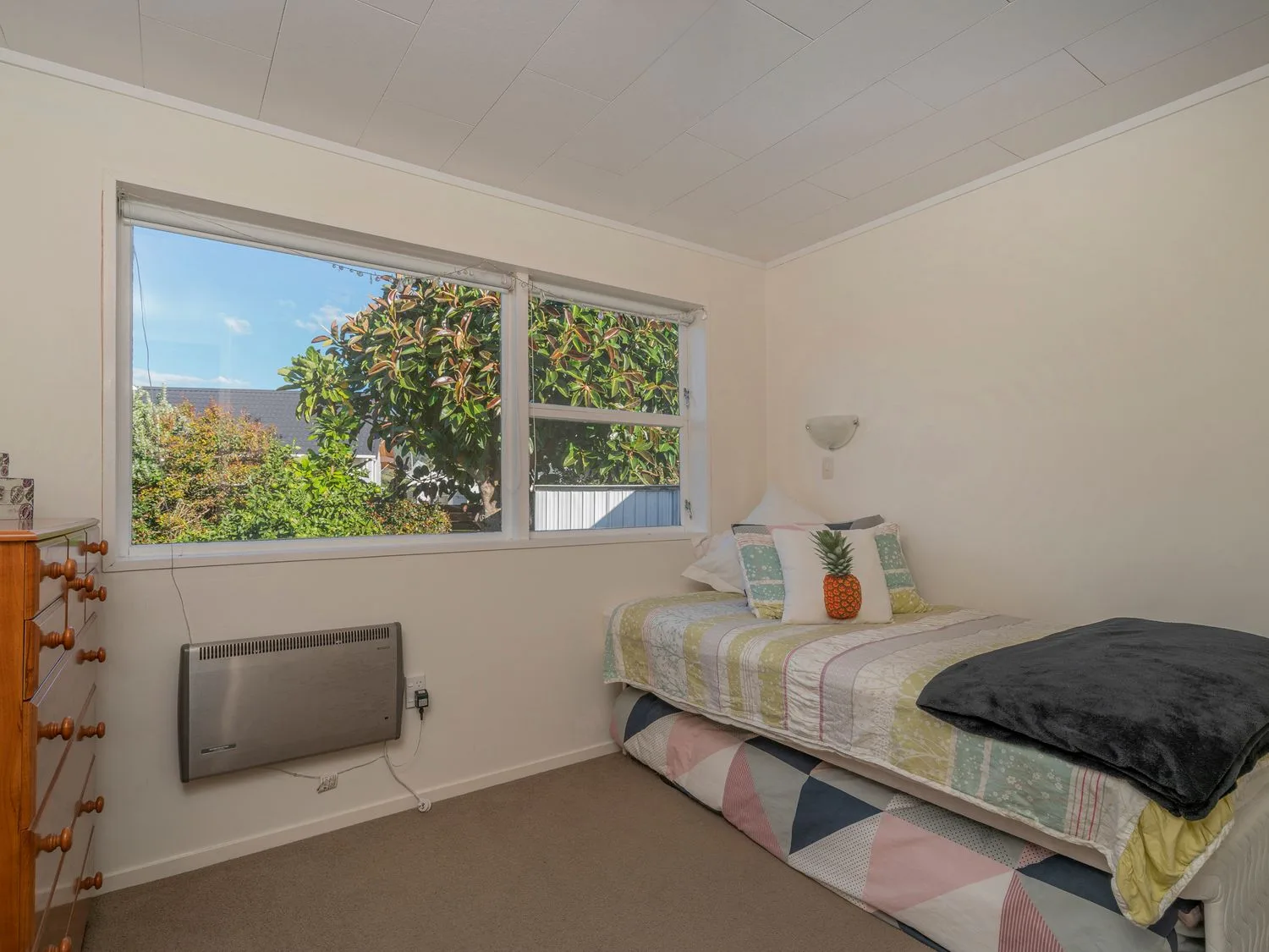 A bedroom with a single bed and a chest of drawers next to a window with a view of greenery at Slice of Pauanui - Pauanui Holiday Home Paunui
