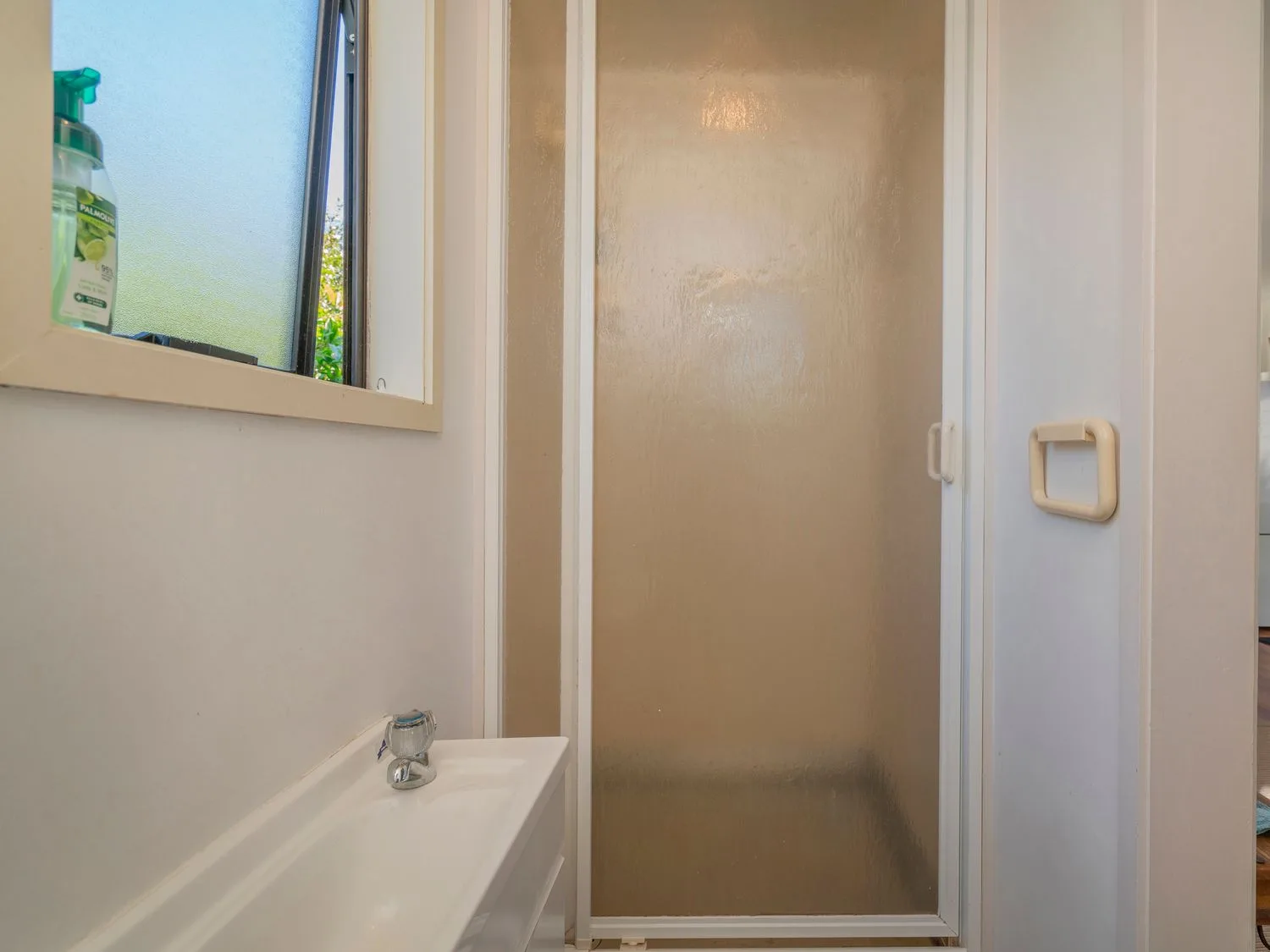 A bathroom with a frosted glass shower and a sink beneath a window.