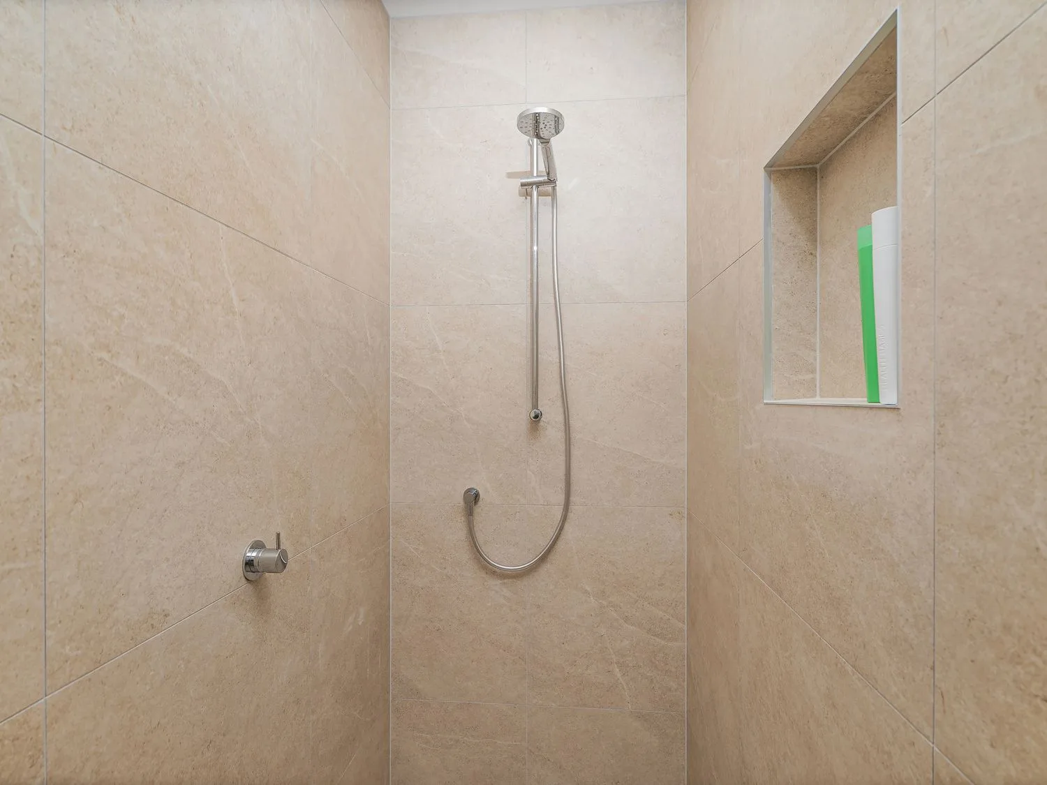 A tiled shower area with a handheld showerhead and recessed wall niche.
