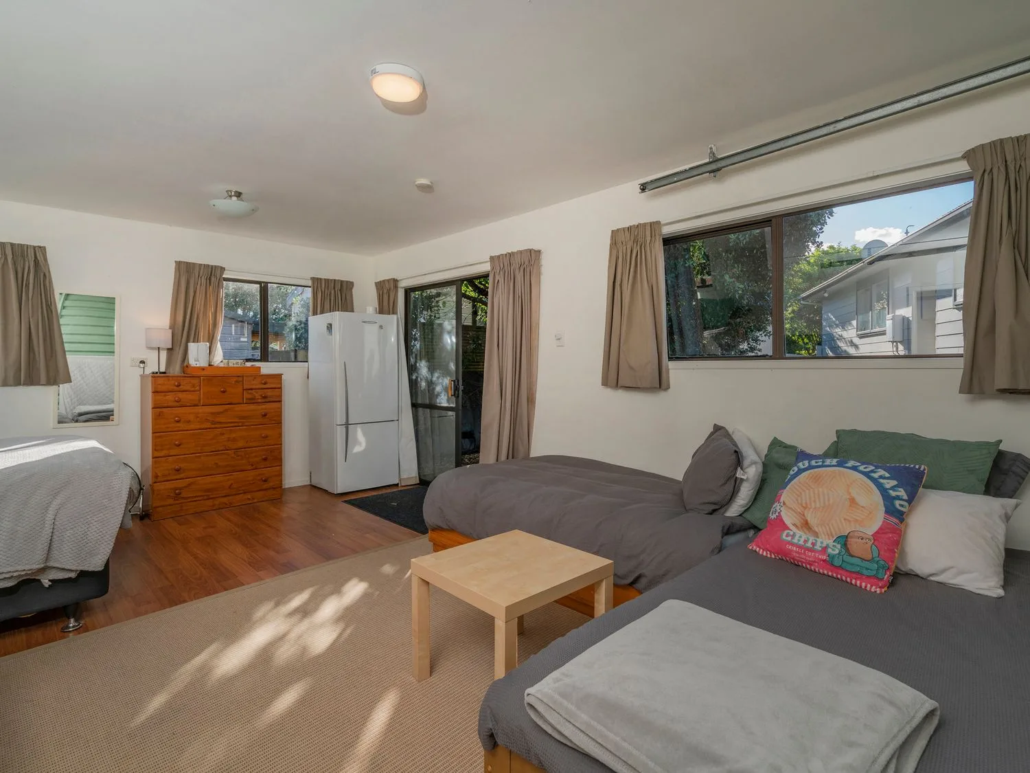 A bedroom with a bed, a dresser, and a refrigerator beside the windows.