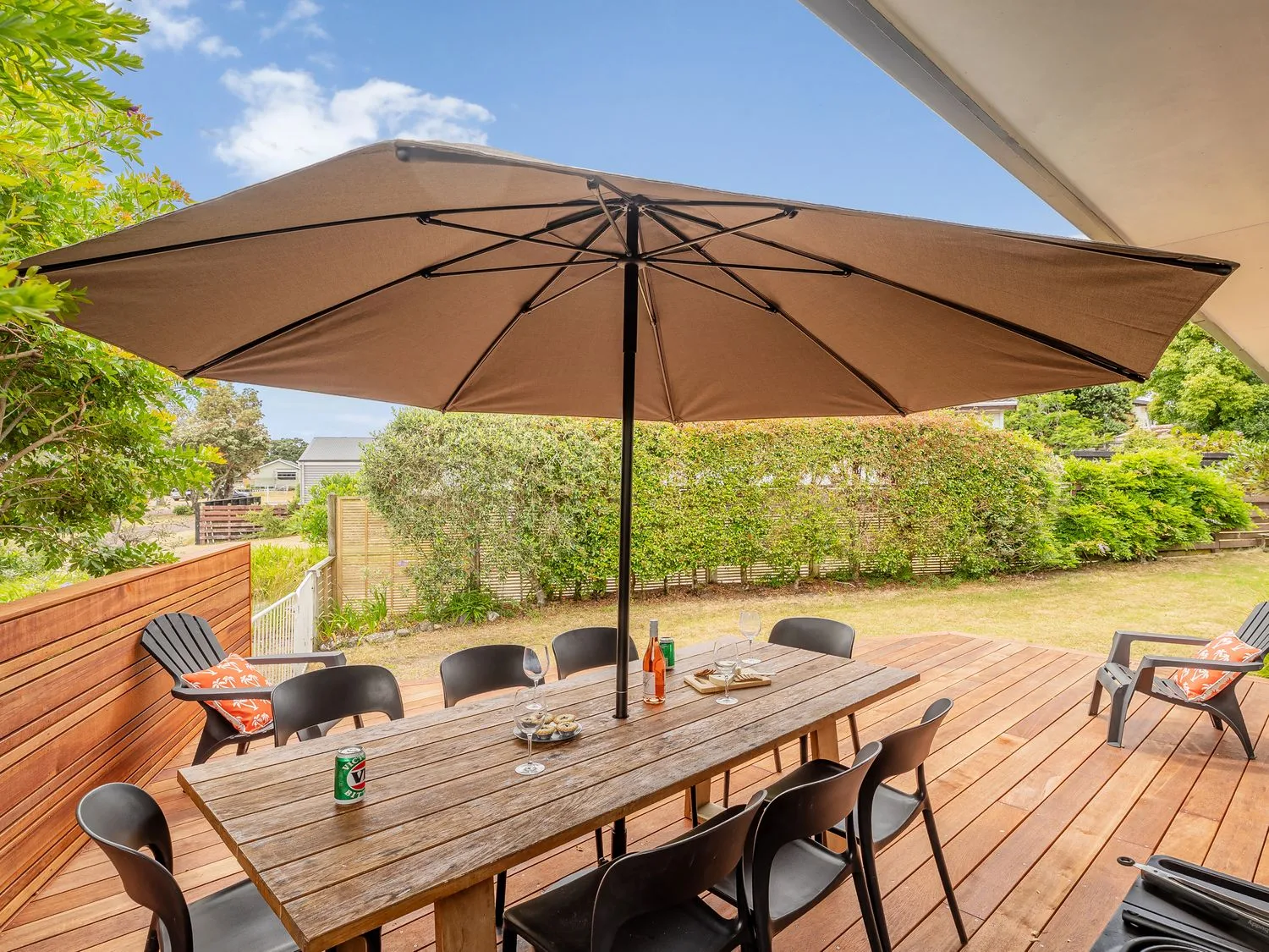 An outdoor dining area on a wooden deck sits beneath a large patio umbrella.