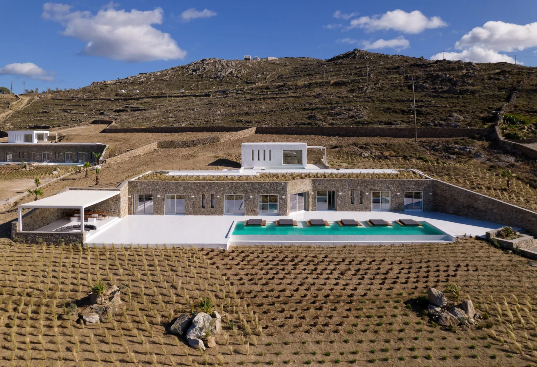A modern villa with a swimming pool sits among terraced hills.