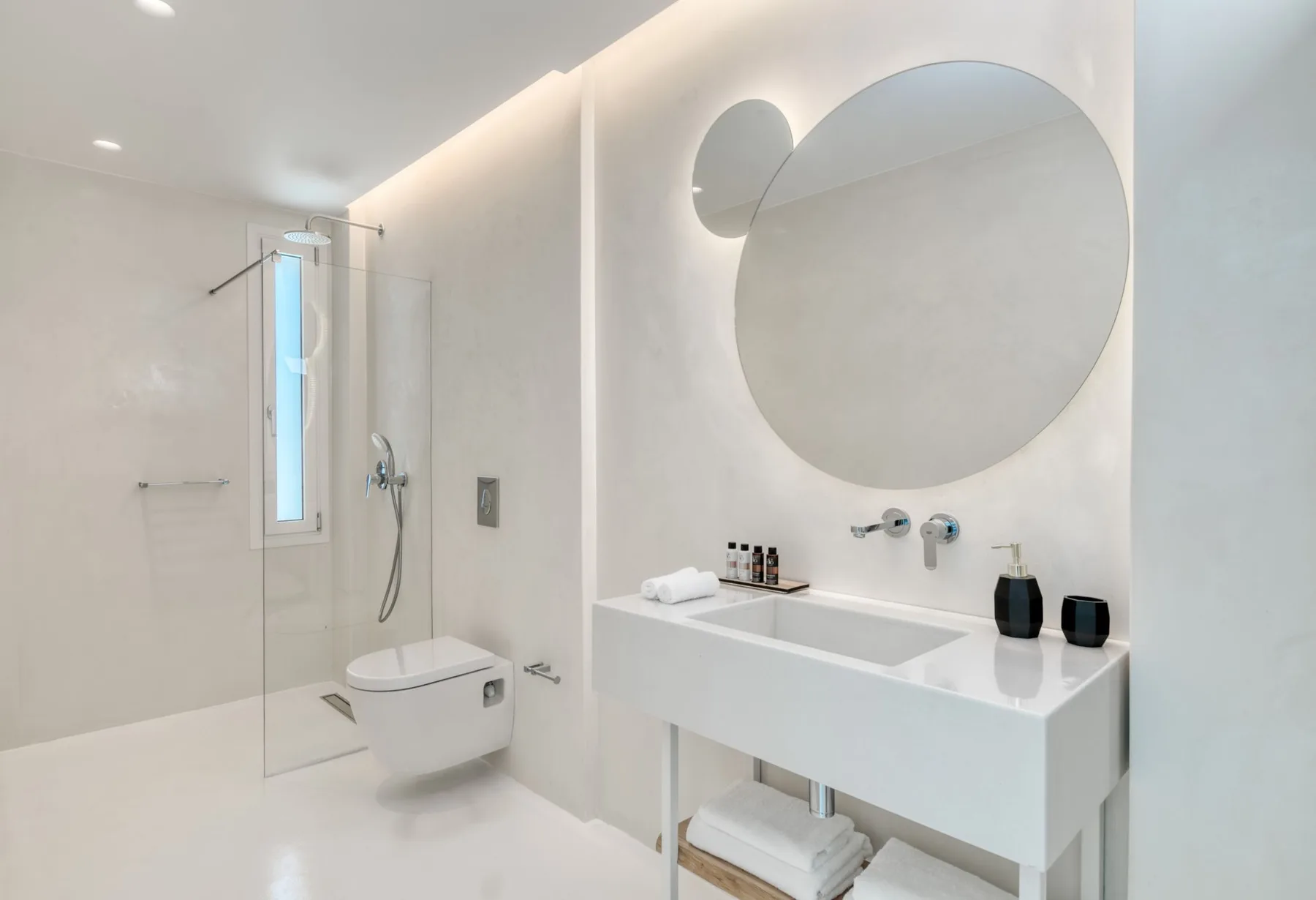A bright bathroom with a glass shower and a large round mirror.