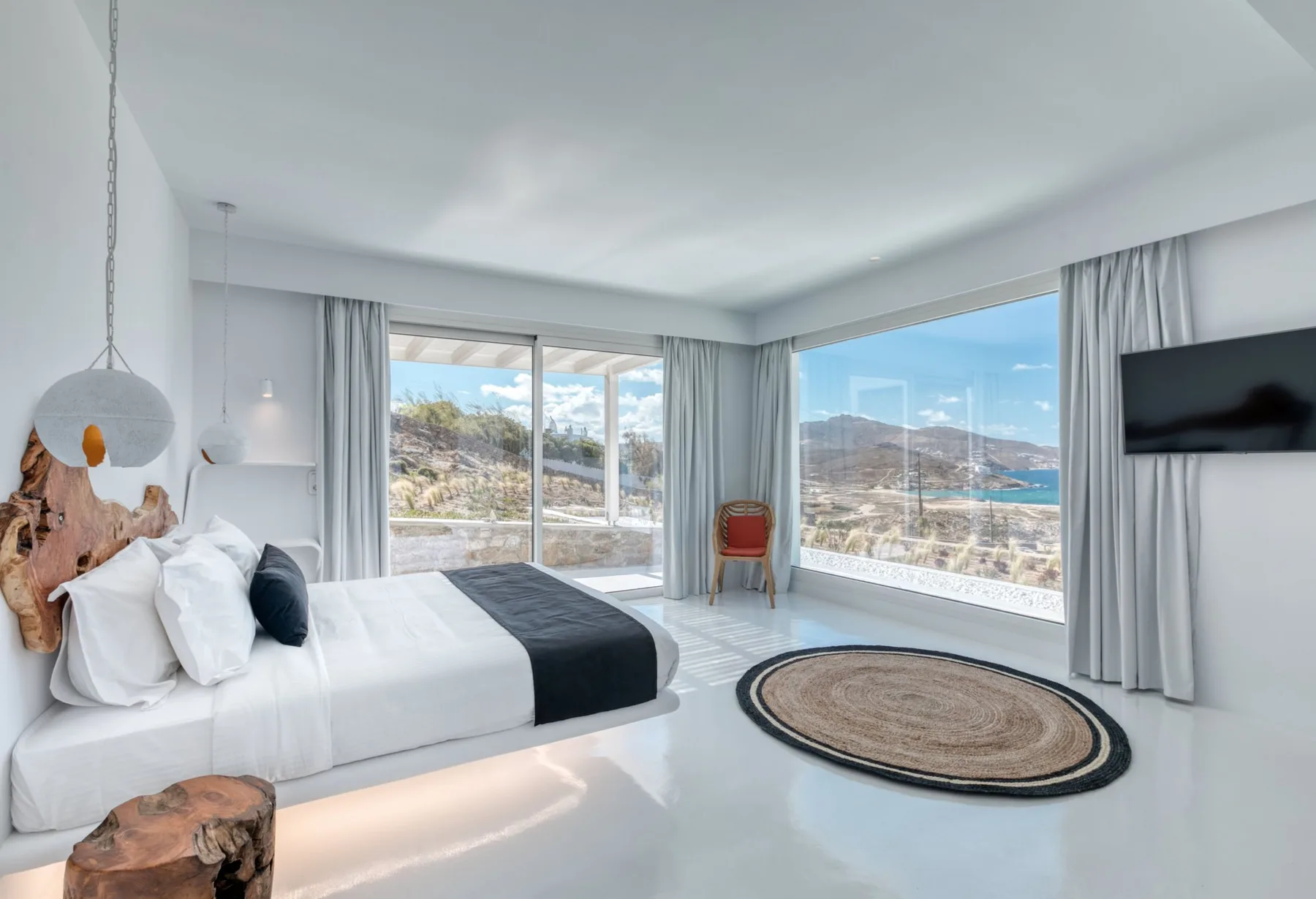 A bright bedroom with a bed and large windows overlooking a mountain landscape.