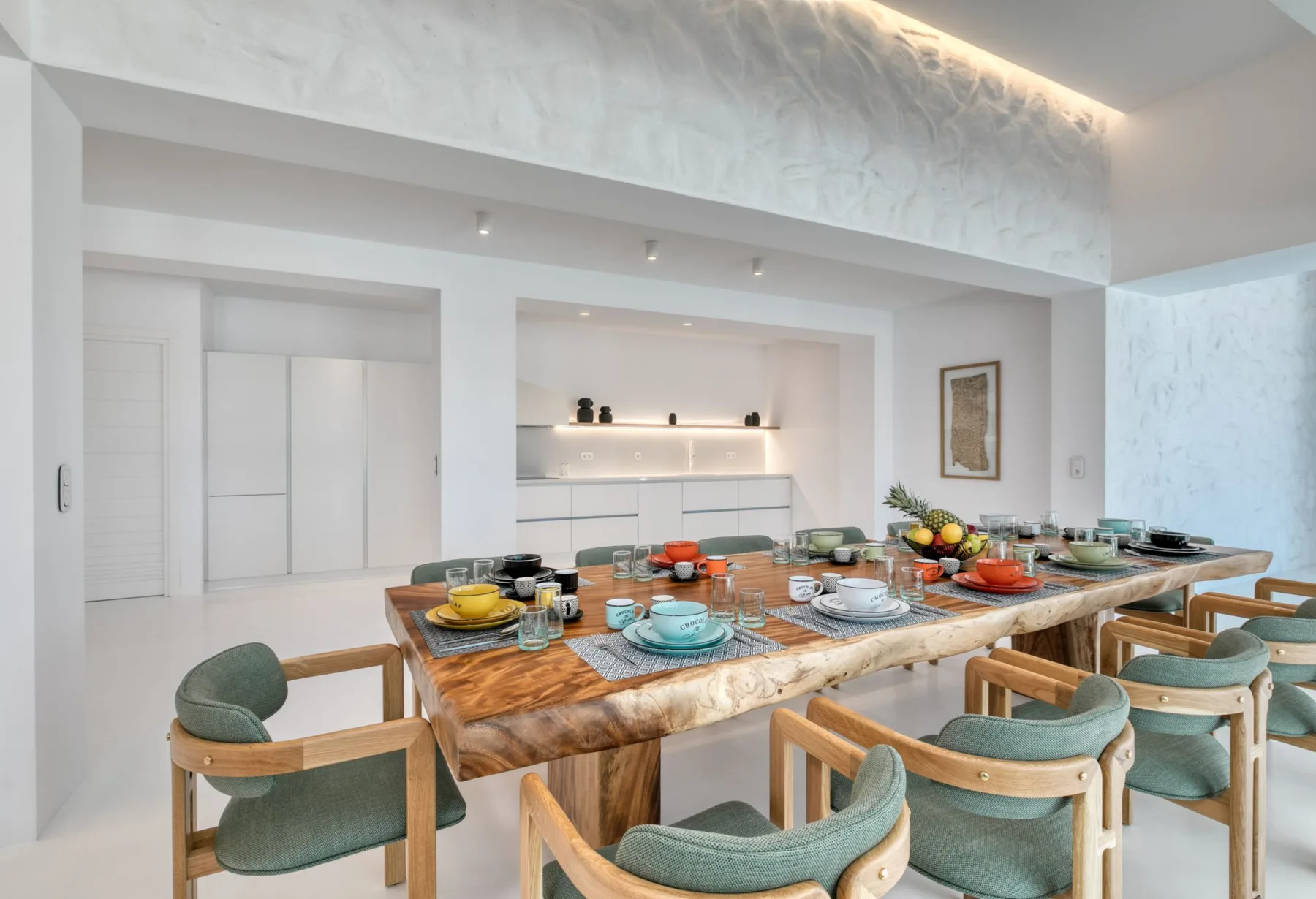A dining area with a long wooden table set with dishes and fruit.