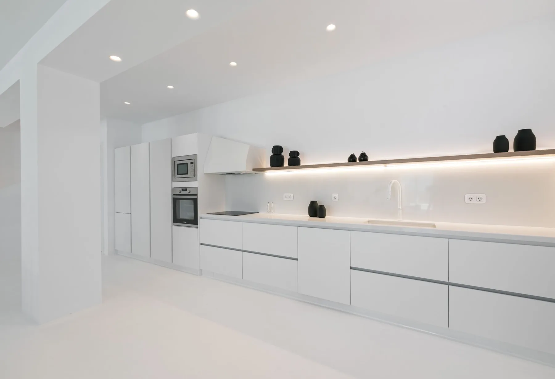 A bright modern kitchen with white cabinets and a long countertop.
