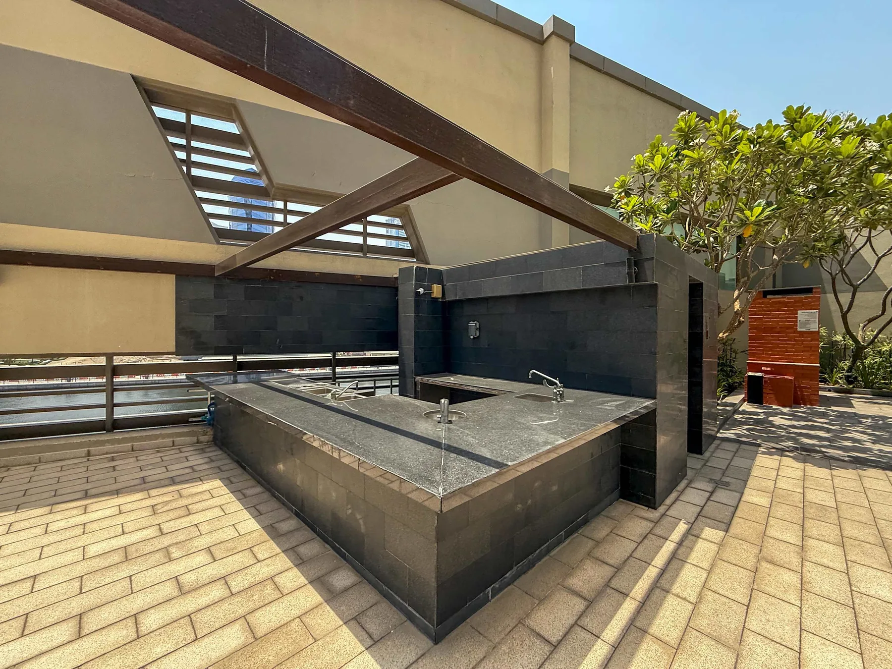 Una fuente de piedra al aire libre está bajo una pérgola de madera en una terraza pavimentada.