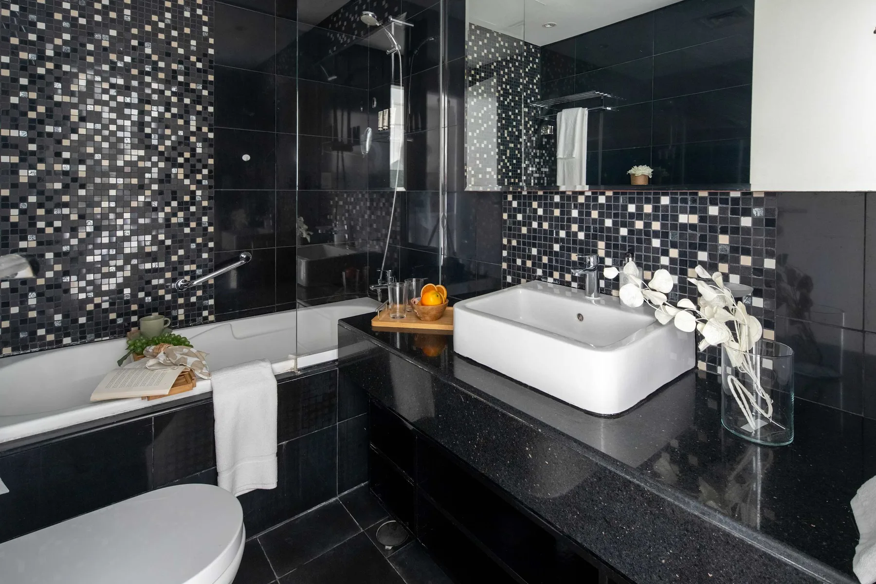 Un baño con bañera, lavabo y paredes de azulejos oscuros.