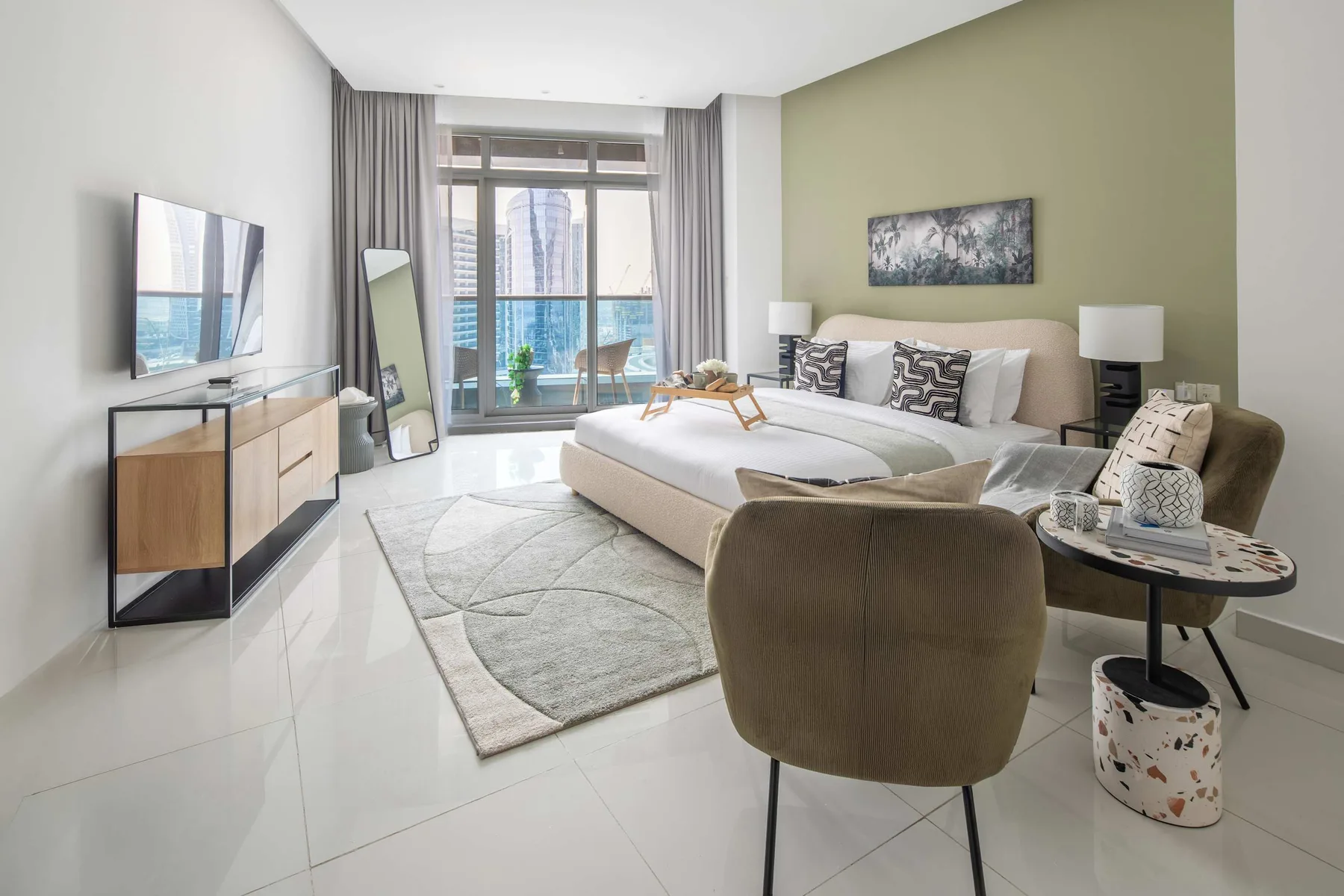 A bright bedroom with a bed, a seating area, and large windows.