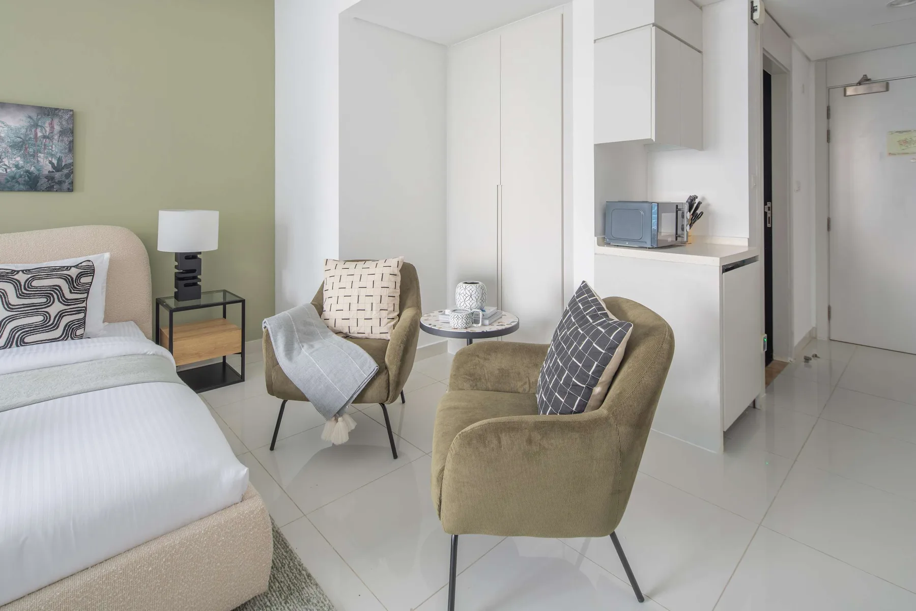 Una zona de estar en un dormitorio con dos sillones junto a la cama.