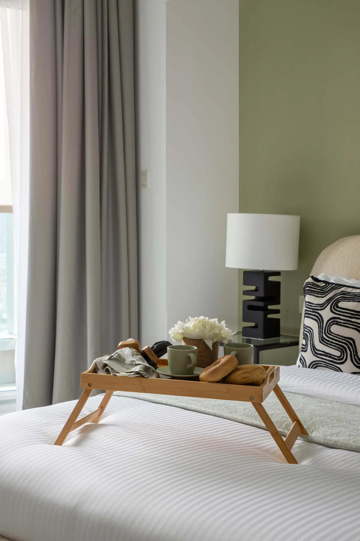 Un dormitorio con una bandeja de desayuno de madera sobre una cama bien tendida.