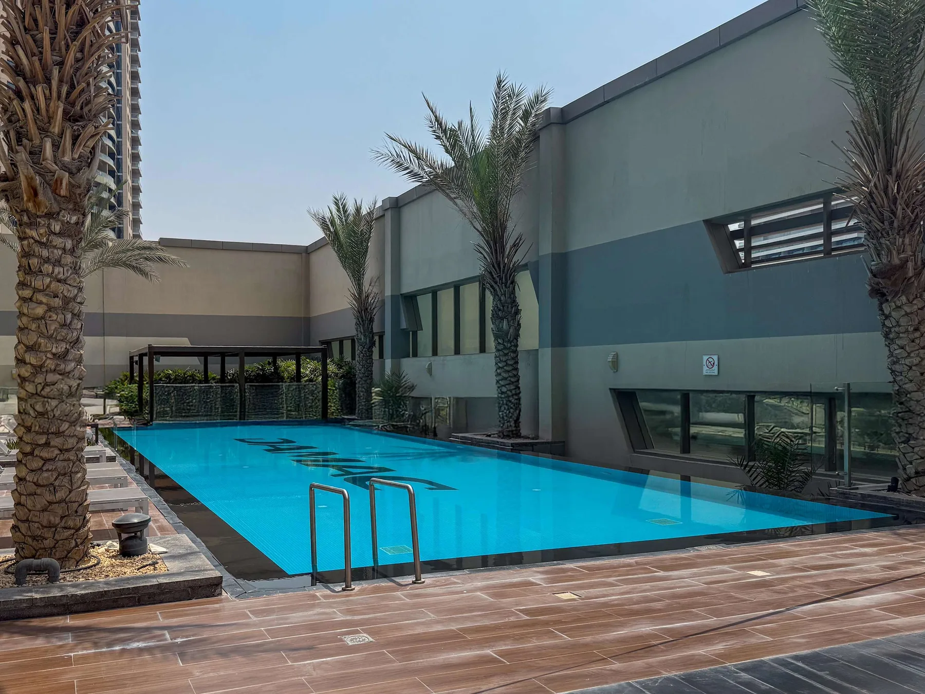 Una piscina al aire libre junto a un edificio moderno, con palmeras en el borde.