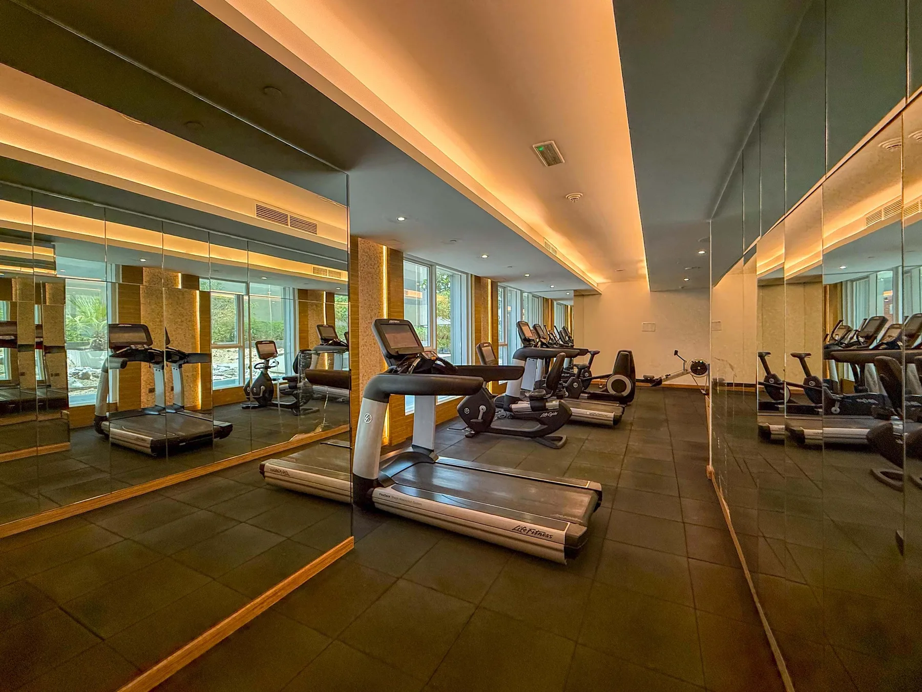 Un gimnasio con cintas de correr y equipo de ejercicio reflejados en paredes con espejos.