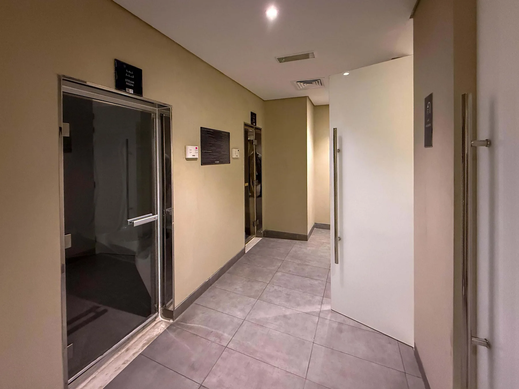 Un pasillo embaldosado con puertas de vidrio oscuro y una puerta blanca abierta.