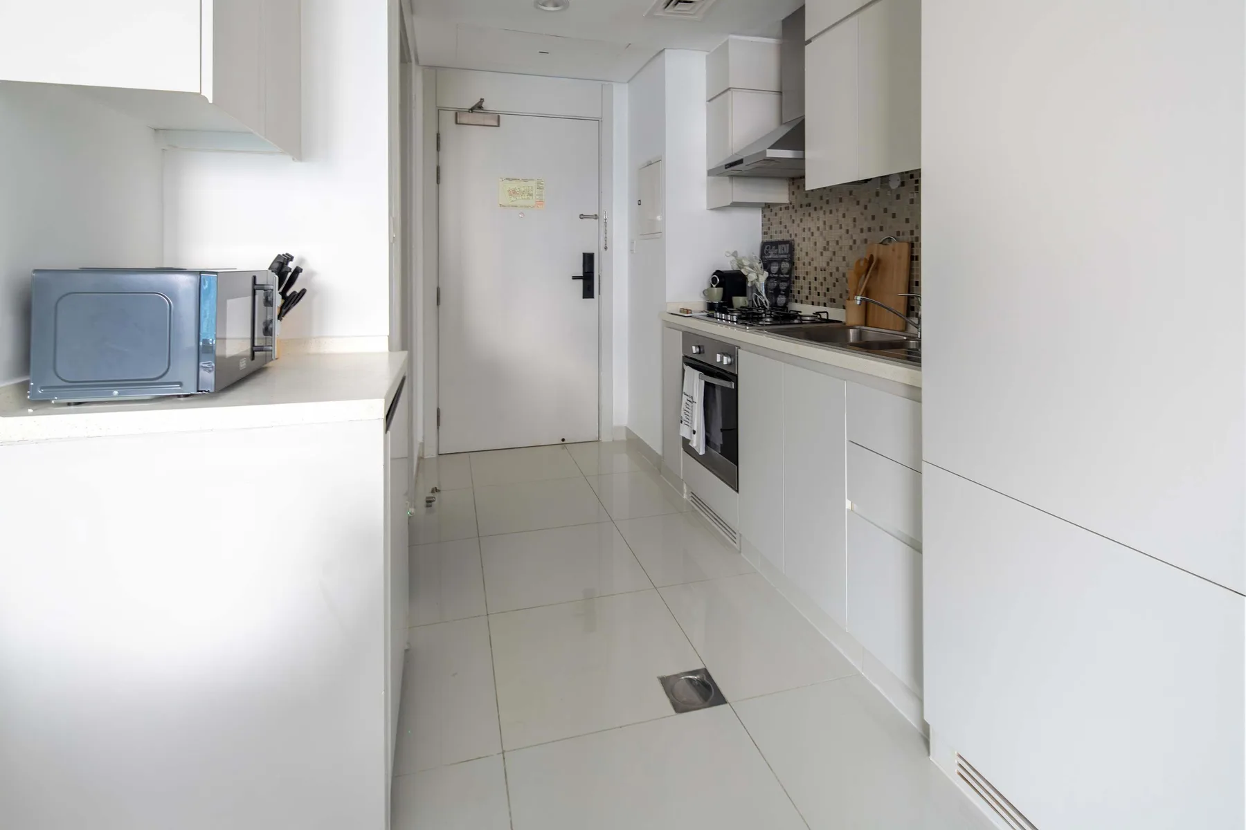 Una cocina estrecha y blanca con armarios, una encimera y electrodomésticos integrados.