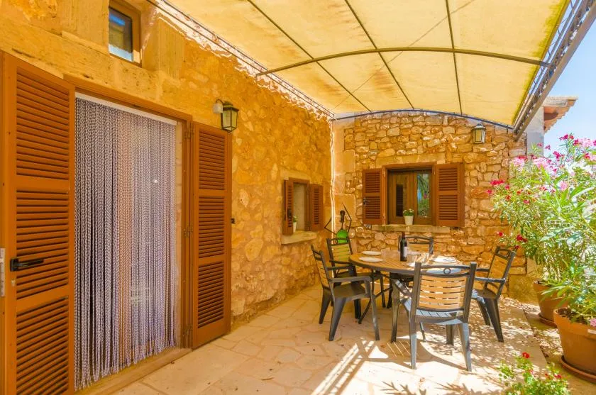 Un patio con paredes de piedra, toldo, asientos al aire libre y plantas con flores.