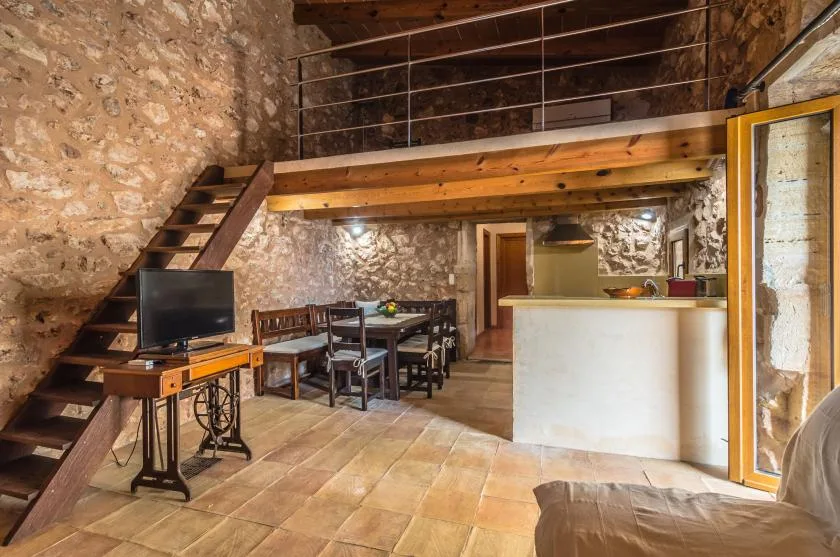 Un interior rústico de piedra con una mesa de comedor bajo un altillo de madera.