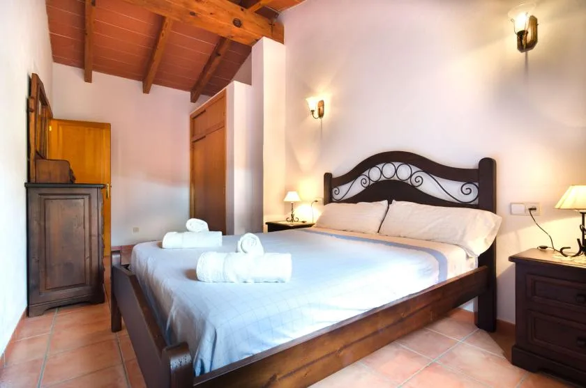 Un dormitorio con una cama doble, ropa de cama blanca y vigas de madera vistas en el techo.