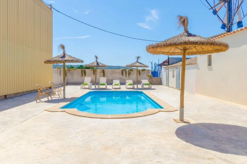 Una piscina al aire libre está en un patio pavimentado bajo sombrillas de paja.