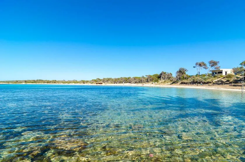 Una bahía azul y clara con aguas poco profundas y una orilla arenosa.