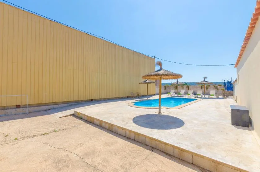 Una piscina al aire libre está en un patio pavimentado bajo una sombrilla de paja.