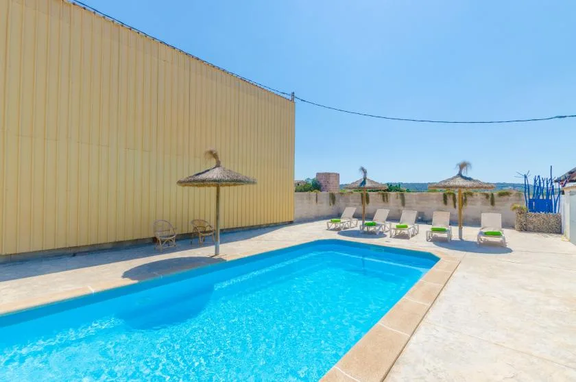 Outdoor pool beside a paved deck with lounge seating and a parasol.