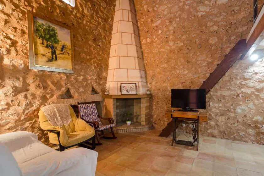 Una sala de estar rústica de piedra con asientos junto a una chimenea alta.