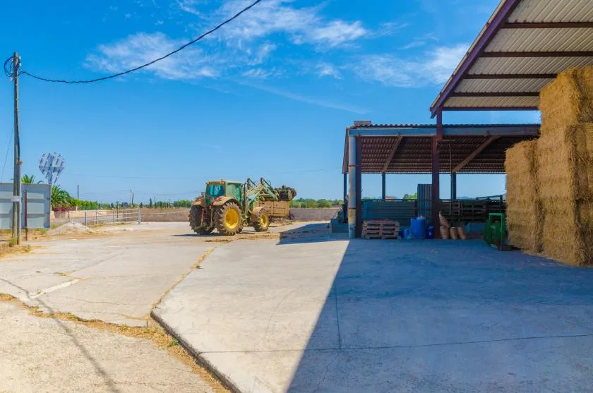 Un patio agrícola de concreto con un tractor junto a cobertizos abiertos.