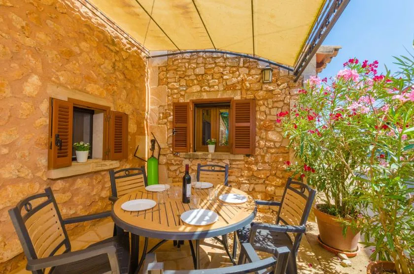 Un comedor exterior con paredes de piedra tiene una mesa redonda bajo un toldo.