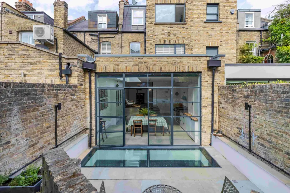 A brick courtyard features a glass-walled dining area beside a small pool.