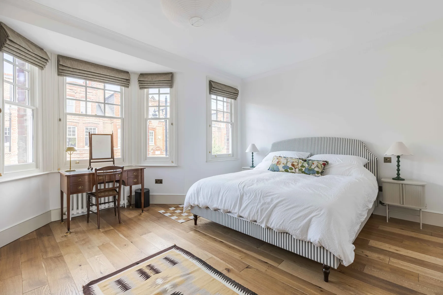 A bright bedroom with a large bed and a desk beside the windows.