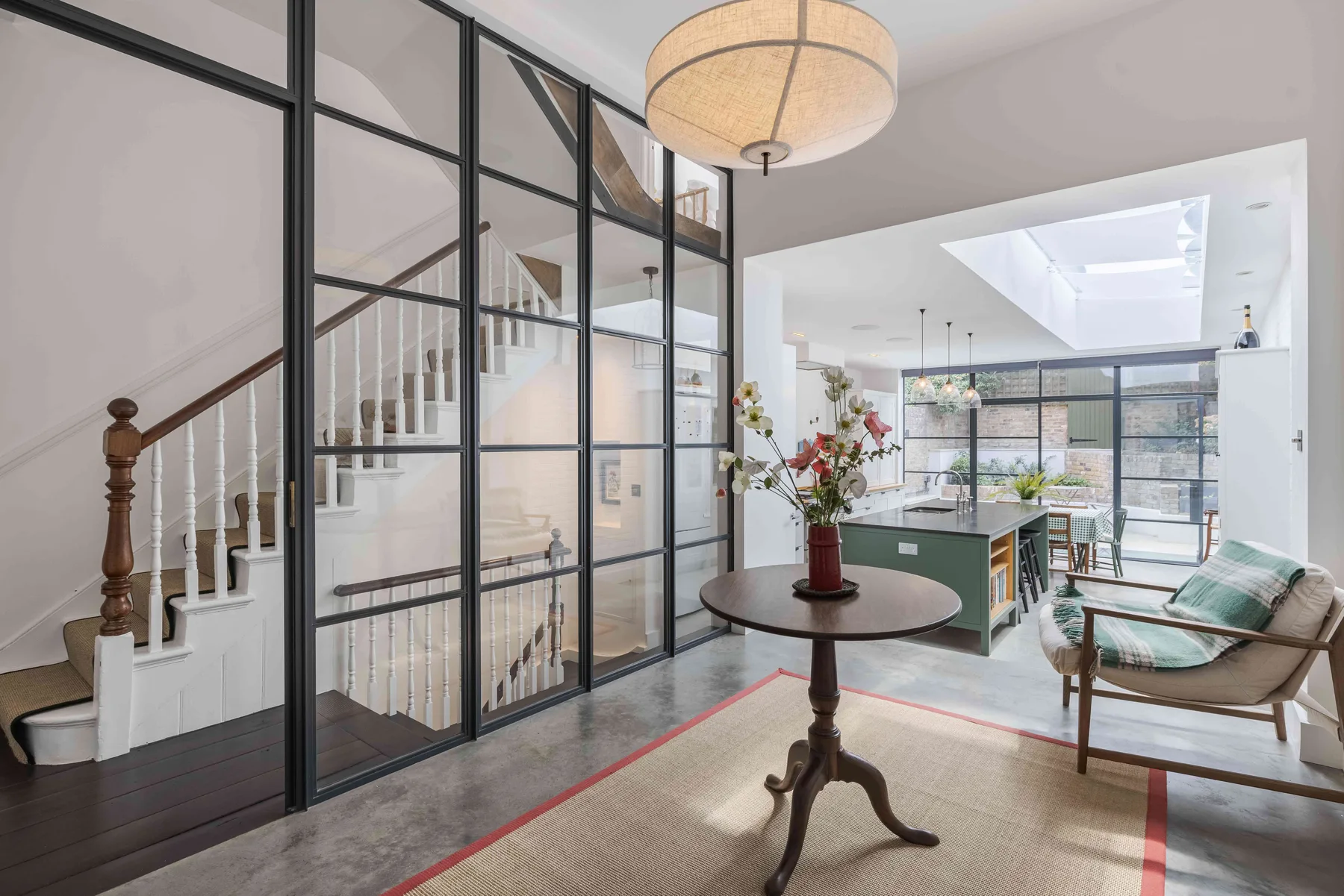 A bright open-plan living and kitchen area with a staircase behind glass partitions.