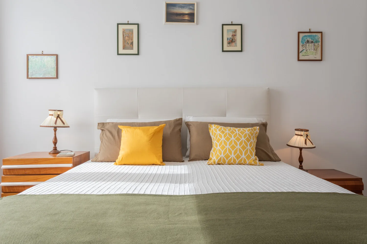 Un dormitorio con una cama bien hecha, cojines amarillos y lámparas de mesilla.