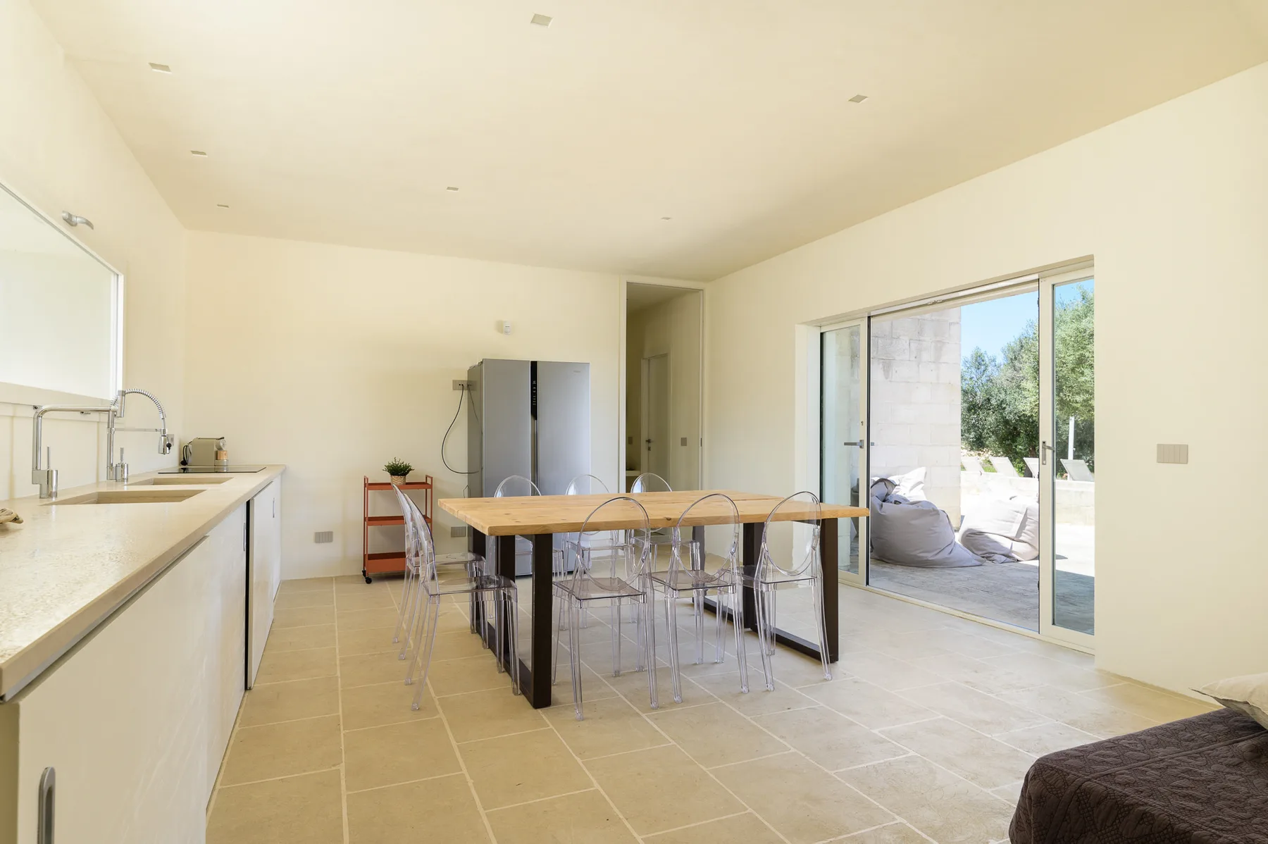 A bright kitchen and dining area with a long table beside sliding glass doors.