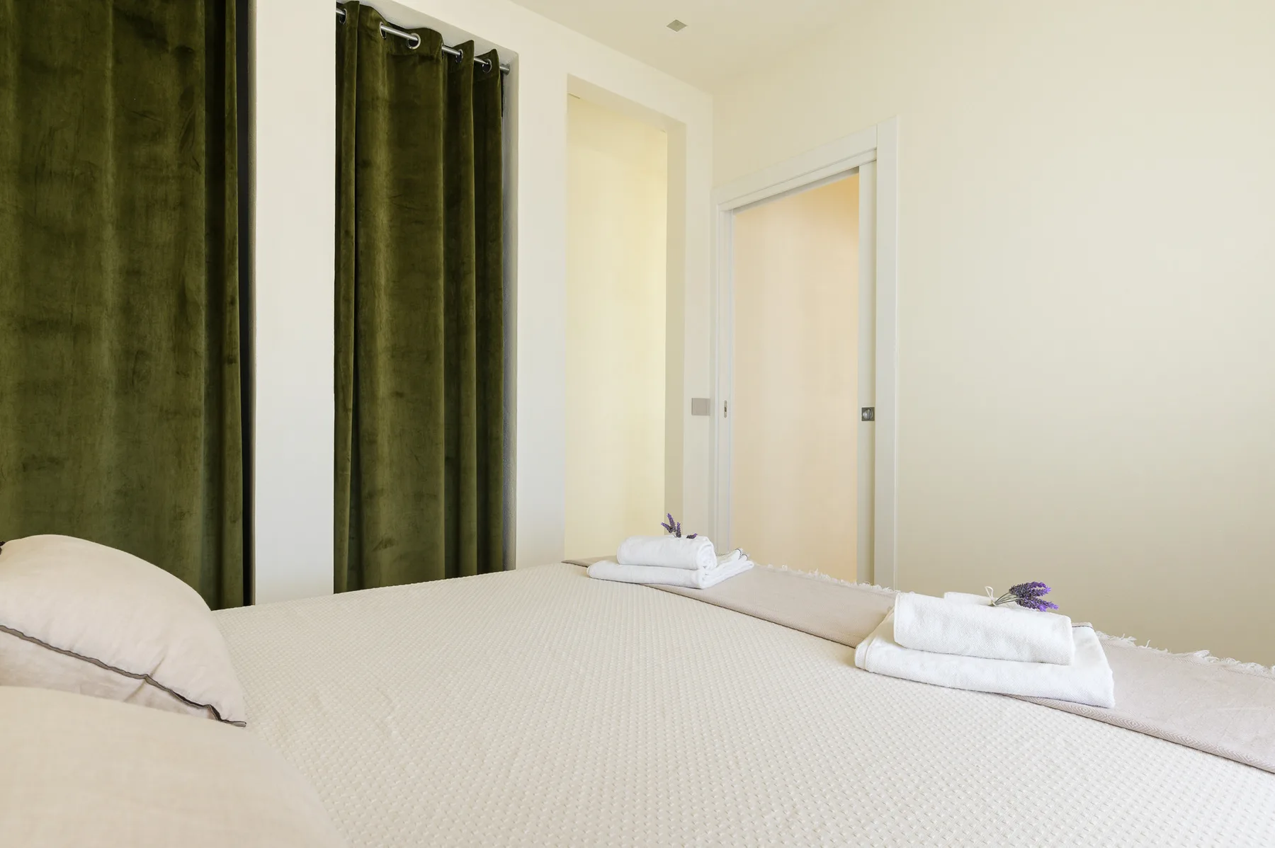 A bedroom with a neatly made bed and dark curtains.