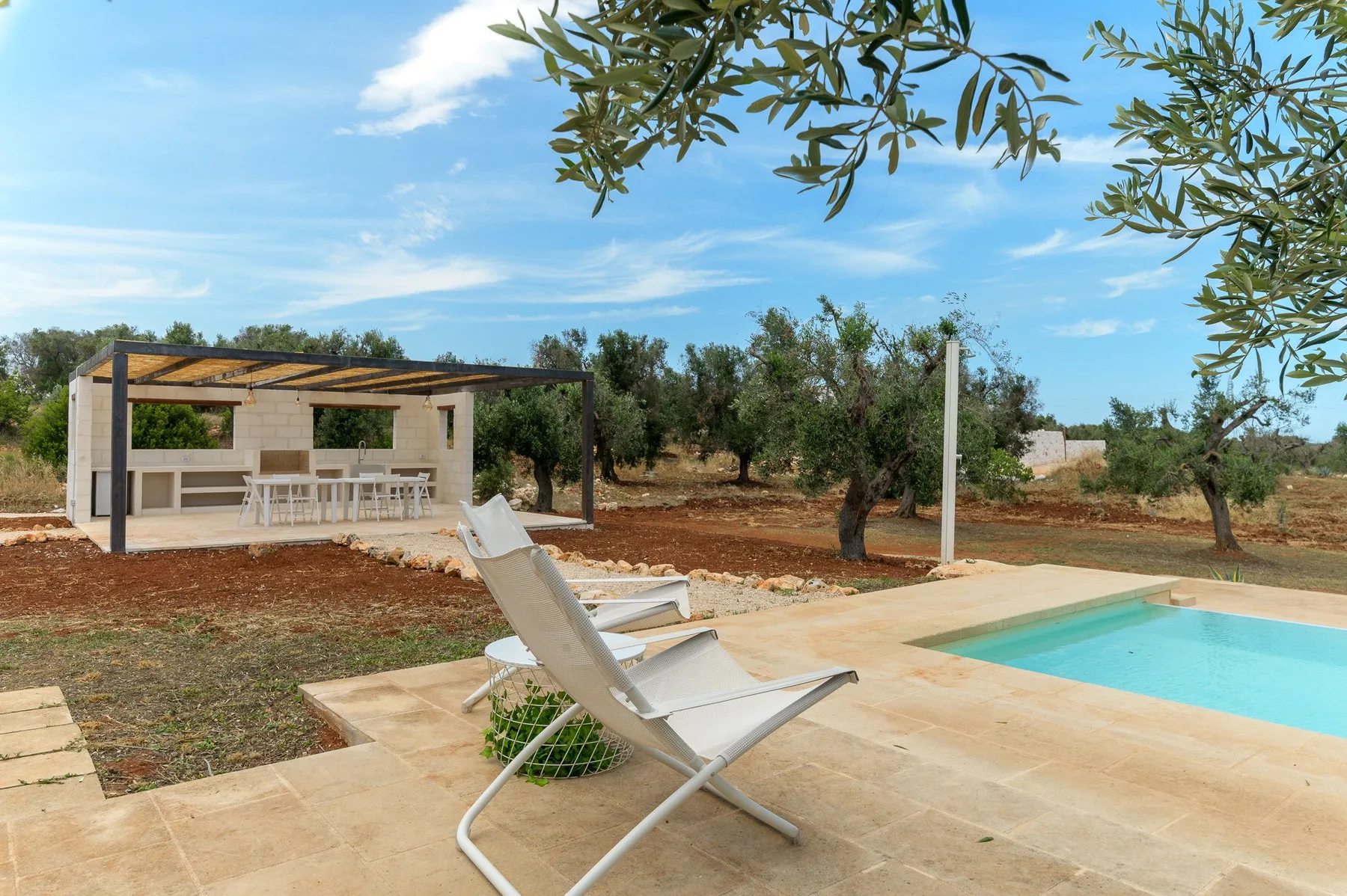 An outdoor swimming pool beside a shaded patio with seating and a reclining chair.