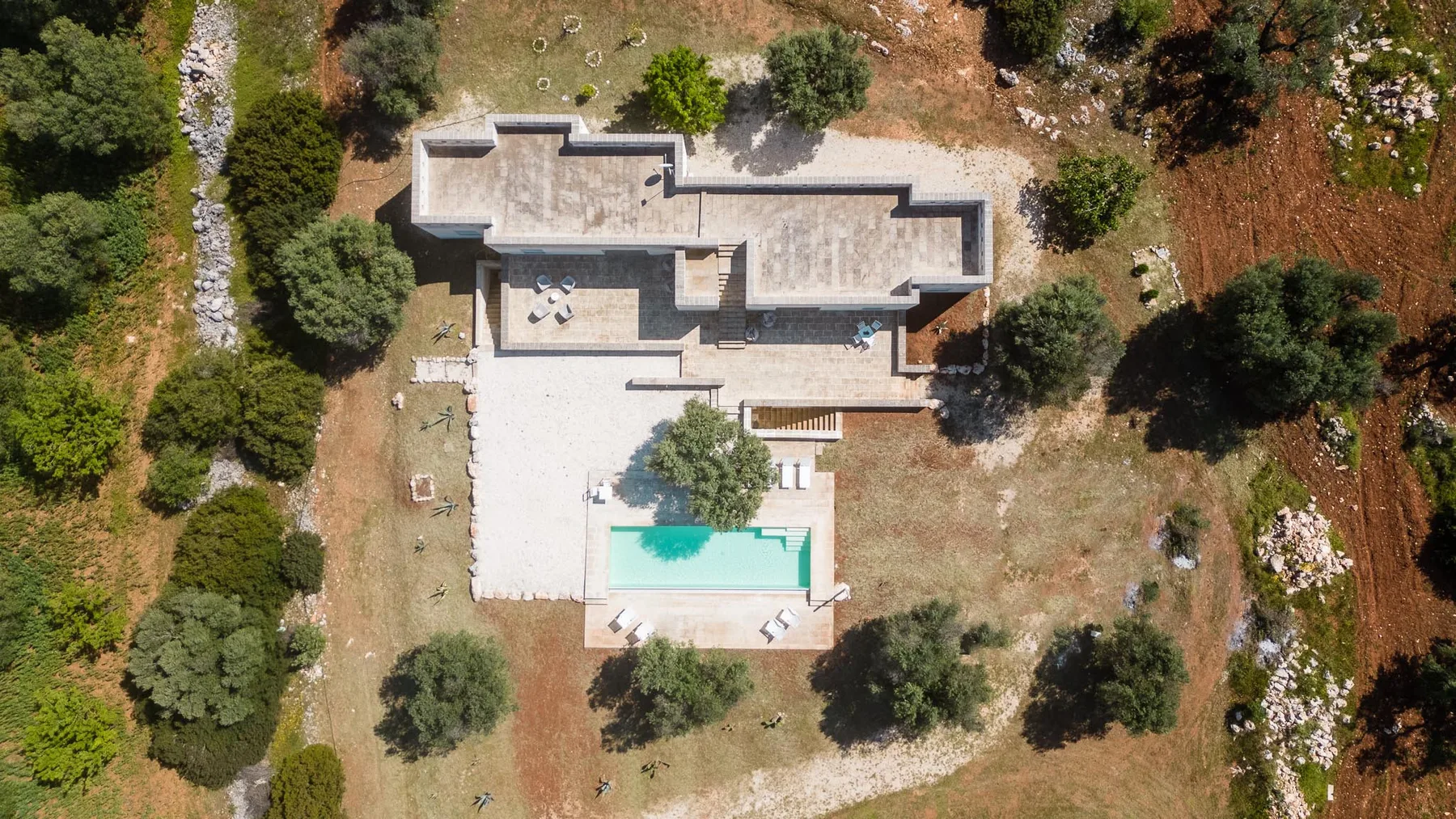 An aerial view of a modern building beside a swimming pool and surrounding trees.