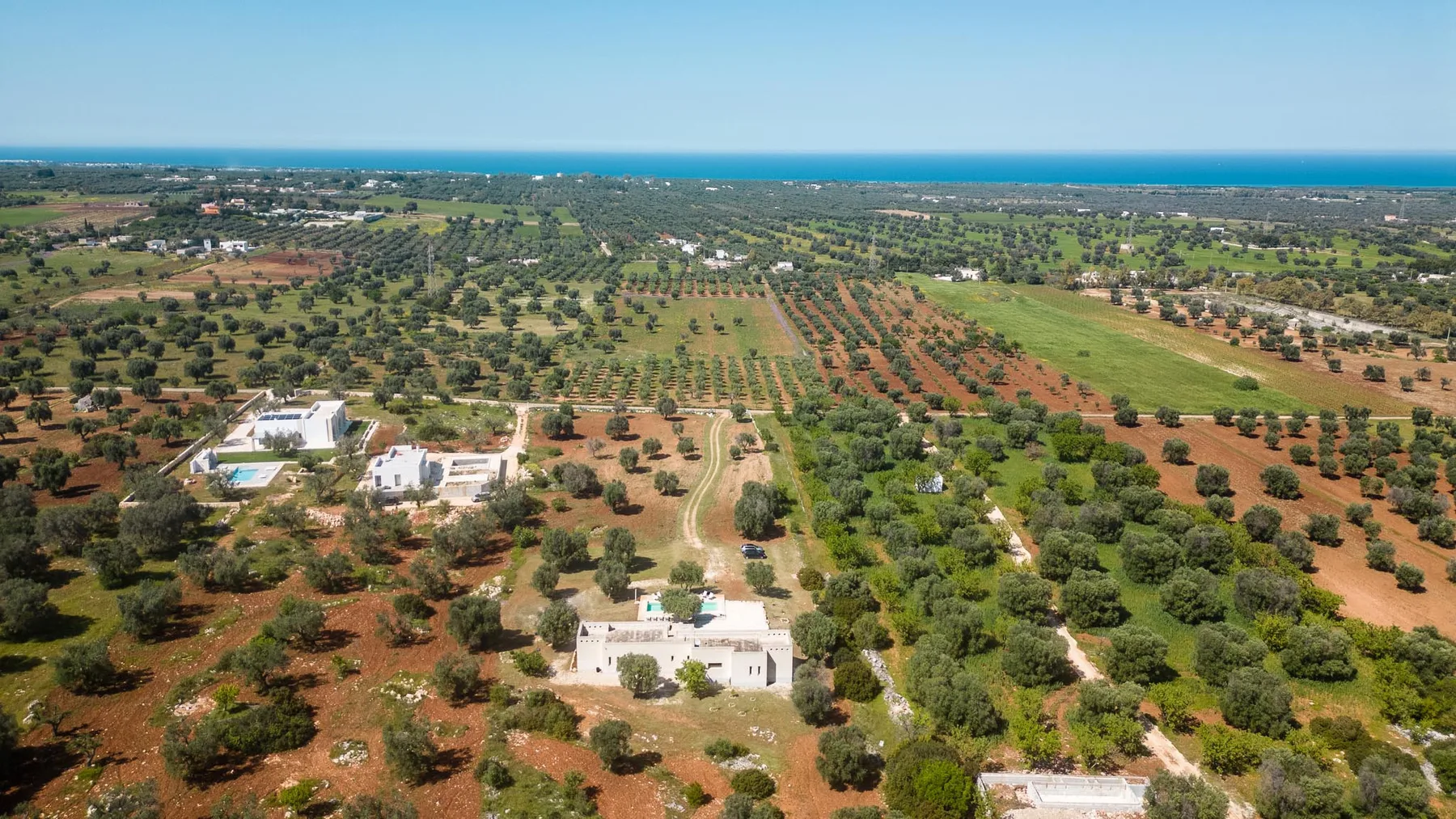 An aerial view of agricultural fields and scattered buildings beneath a clear sky.