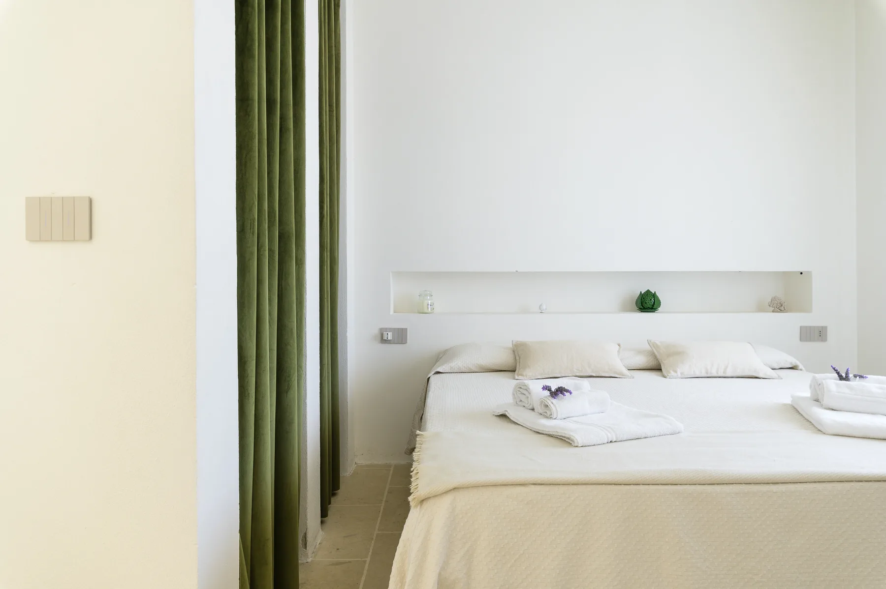 A bright bedroom with a neatly made bed and green curtains.